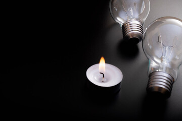 Electric lamp and candle on a dark background.  Incandescent bulb and candle. Power cut or power...