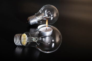Electric lamp and candle on a dark background.  Incandescent bulb and candle. Power cut or power...