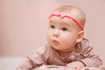 Portrait of a beautiful little girl 6 months old. Close-up of a baby on a bright background in the studio. Beautiful girl with a bow on her hair. Baby care. Children Protection Day.
