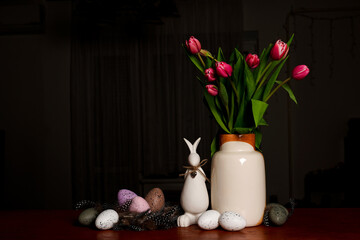 A bouquet of tulips, Easter bunny and eggs on wooden table on Scandinavian-style kitchen. Easter night