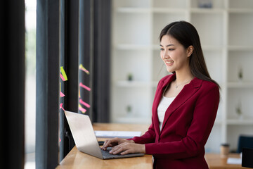 Asian professional businesswoman focusing on her project, typing on laptop computer, sitting in office room.