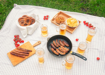 Picnic with beer mugs and glasses, roasted sausages and beer snacks.