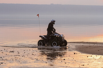 athlete rides a quad bike on the beach at the sunset