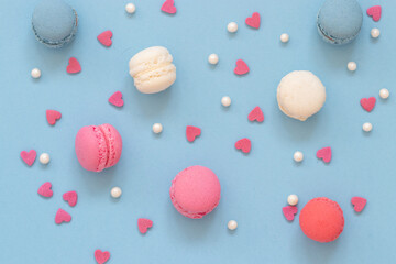 Colorful macaron cookies with heart shaped sugar candies arranged on blue background, top view.