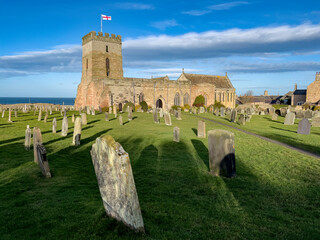 The historic Bamburgh Parish Church and cemetery in the coastal village of Bamburgh in...