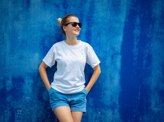 Female model wearing white blank t-shirt on the background of an blue wall.