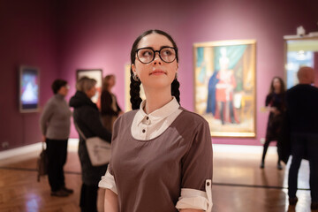 Portrait of young Caucasian pretty woman contemplates arts. Student visiting gallery or museum....