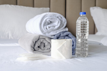 Obraz na płótnie Canvas On the made bed are three towels folded into rolls, a bottle of drinking water and toilet paper. Room service at the hotel. Replacing towels and providing hotel guests with hygiene products.