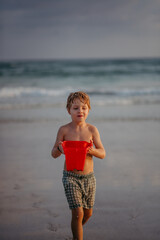 Fototapeta na wymiar Little boy in swimsuit with bucket running out of sea, enjoying holiday.