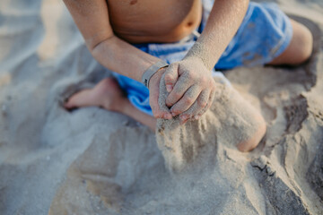 Little boy playing on the beach, sitting in a sand.