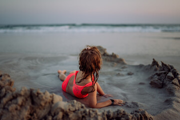 Little girl playing on the beach, digging hole in sand.