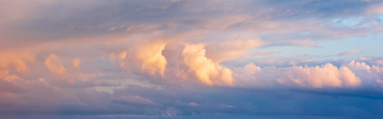 Panoramic background of evening sky with strom clouds glowing in the light of the setting sun
