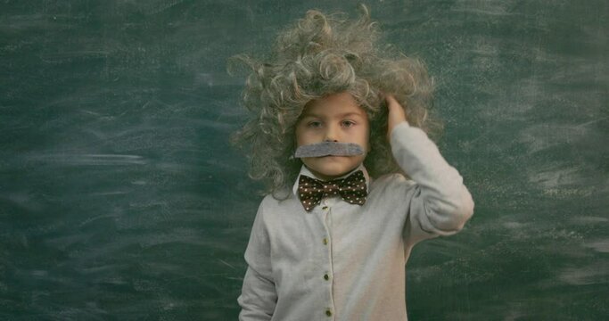 Cheerful smiling little kid (boy) against chalkboard.  Little Einstein style. School and idea concept