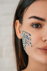 Portrait of a half face of a beautiful girl with a pull-up tape on her face. Kinesio-taping. The concept of facial skin care