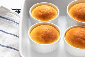 Freshly baked golden souffle desserts in ceramic jars, right after baking on white baking tray