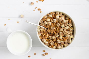 Breakfast cereals in a white bowl with a glass of milk. White table, top view