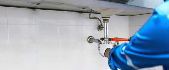 Technician plumber using a wrench to repair a water pipe under the sink. Concept of maintenance,...