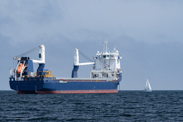 Huge cargo ship and small sailboat in the open sea. Concept of difference, diversity and distinction