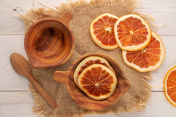 Several dry grapefruit slices with two wooden cups and jute napkin on wooden table, macro, top view.