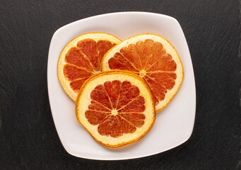 Fototapeta na wymiar Three dry grapefruit slices with white saucer on slate stone, macro, top view.