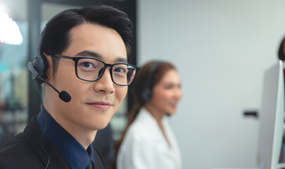 Asian call center agent team, customer service support wearing headset or headphone talking with customer in modern office.