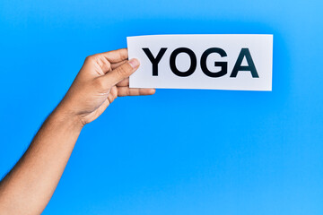 Hand of caucasian man holding paper with yoga word over isolated blue background