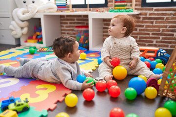Fototapeta na wymiar Two adorable babies playing with balls sitting on floor at kindergarten