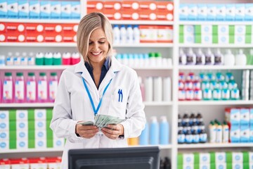 Young blonde woman pharmacist smiling confident counting dollars at pharmacy