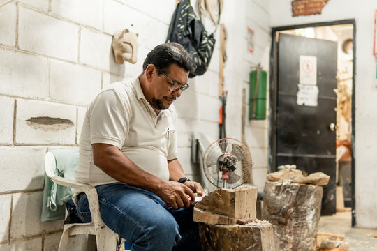 hands of older latino man carving a jaguar in wood with knife with a lot of passion