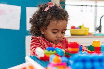 Adorable hispanic girl playing with construction blocks sitting on table at kindergarten