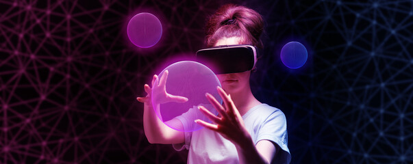 Portrait of young woman in VR glasses creates 3D simulation of pink mesh sphere. Dark background with neon abstracts. Banner with copy space. The concept of virtual reality and metaverse