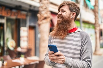 Young redhead man smiling confident using smartphone at street