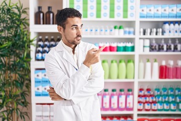 Handsome hispanic man working at pharmacy drugstore pointing with hand finger to the side showing...