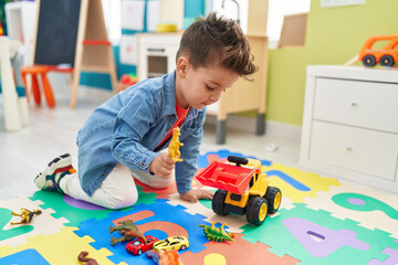 Adorable hispanic toddler playing with tractor and dino toy sitting on floor at kindergarten