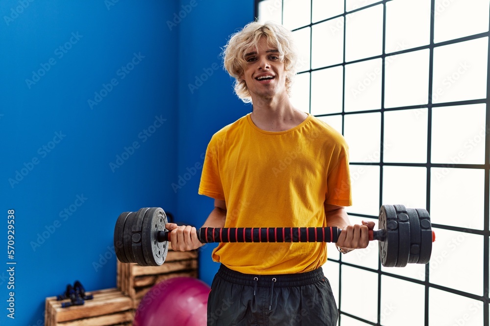 Sticker young blond man smiling confident using weight training at sport center