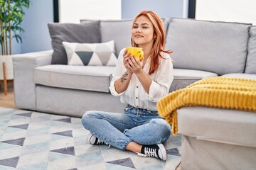 Young caucasian woman drinking coffee sitting on floor at home