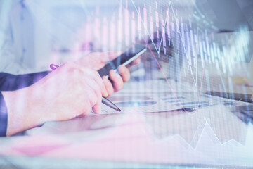 Double exposure of man's hands holding and using a phone and financial chart drawing. Market analysis concept.