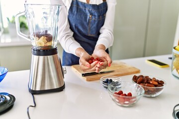 Young blonde woman holding raspberries at kitchen