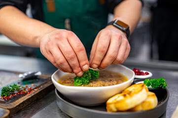 close up of male chef hand serving plate of soup at restaurant kitchen