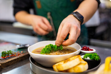 close up of male chef hand serving plate of soup at restaurant kitchen