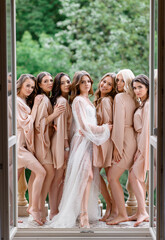 Beautiful bride in elegant wedding dress and bridesmaids dress in beige style robes standing on...
