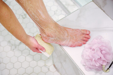 Woman scrubbing foot with sponge in the shower - 570932335