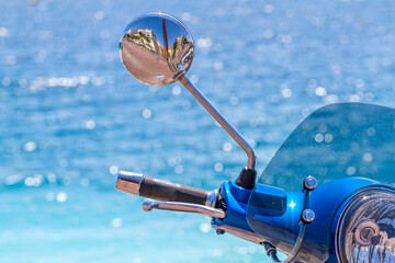 The close up view of chromed handle of motorbike. Empty street reflected in its rear view mirror. Clear blue water on a background