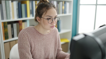 Young beautiful hispanic woman student using computer studying at library university