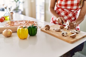 Young beautiful hispanic woman cutting mushroom at the kitchen