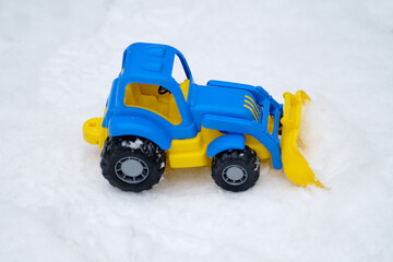 Children's toy tractor lies on the snow in the winter park