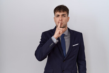 Young hispanic business man wearing suit and tie asking to be quiet with finger on lips. silence...
