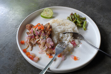 Delicious lunch menu, white rice, chicken meat with chili sauce topping, sliced chili, onion, lemongrass leaves, orange leaves, and others.