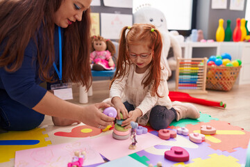 Teacher and student playing with hoops toys sitting on floor at kindergarten