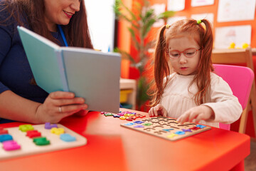 Fototapeta premium Teacher and student playing with maths puzzle game reading book at kindergarten